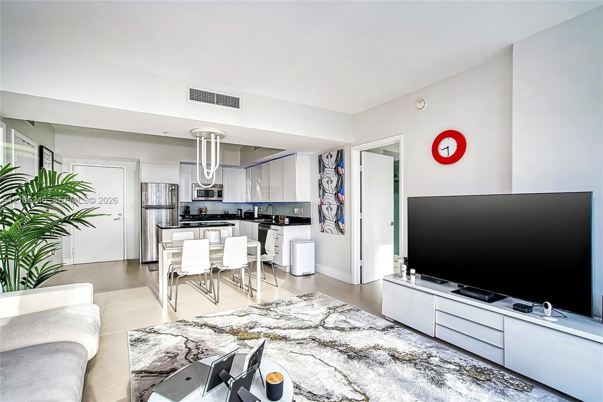 Open-concept kitchen featuring high-gloss white cabinetry, contrasting dark countertops, stainless steel appliances, and a modern sculptural pendant l