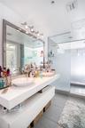 Floating white vanity with dual vessel sinks, large framed vanity mirror, and walk-in glass-enclosed shower with frosted privacy glass and oversized t