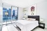 Floor-to-ceiling glass sliding doors, private balcony with glass railing, large-format tile flooring, and custom built-in shelving unit
