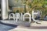 Exterior entrance featuring brushed metal structural columns, stone-textured facade wall, sculptural metal signage, and gravel landscaping with integr