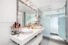 Floating dual-vanity with rectangular vessel sinks, expansive wall-to-wall mirror, overhead track lighting, and a walk-in shower enclosed by frosted g