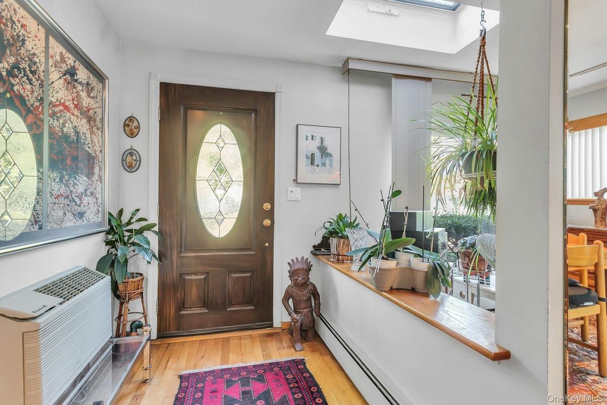 Hardwood flooring, wood-panel entry door with decorative glass inlay, overhead skylight, and half wall with wood ledge