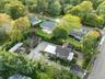 Stone facade residence featuring a dark shingle roof, extensive paved driveway, mature landscaping, and an attached garage
