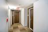 Hallway featuring neutral wall finishes, tile-patterned carpeting, and wood-finish doors set within contrasting dark wood-toned surrounds