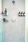 Shower stall featuring large-format light gray tile, a chrome rainfall showerhead, a single-handle chrome pressure balance valve, and two integrated g