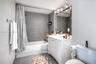Bathroom featuring a white vanity cabinet with a solid surface countertop, an expansive framed vanity mirror, multi-bulb overhead lighting, and a show