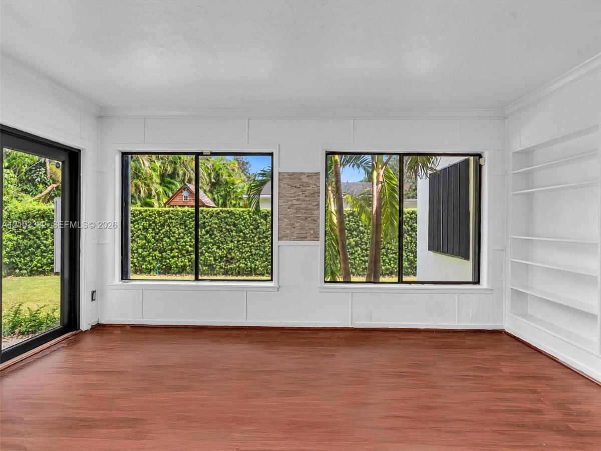 Florida room featuring wood-finish flooring, white panel-style wall detailing, large sliding glass doors, dual windows with black frames, and custom b