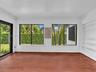 Florida room featuring wood-finish flooring, white panel-style wall detailing, large sliding glass doors, dual windows with black frames, and custom b