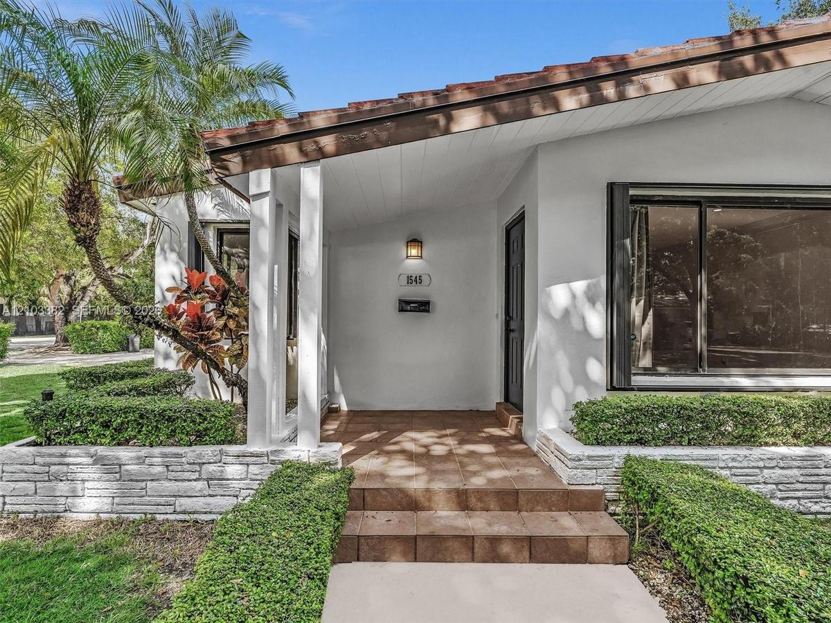 Exterior featuring a covered entryway with ceramic tile steps, white stucco siding, stacked stone landscaping walls, and a large picture window. House