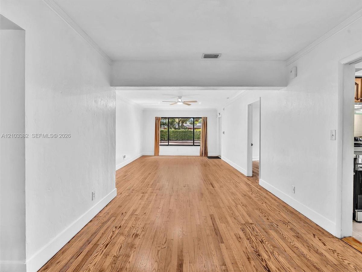 Open-concept split interior featuring wood-finish flooring, crisp white wall finishes, crown molding, ceiling fans. House for rent in Coral Gables. Ho