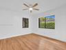 East rear bedroom. Wood-finish flooring, white walls, dual windows with black frames, and a ceiling-mounted fan with integrated lighting. House for re