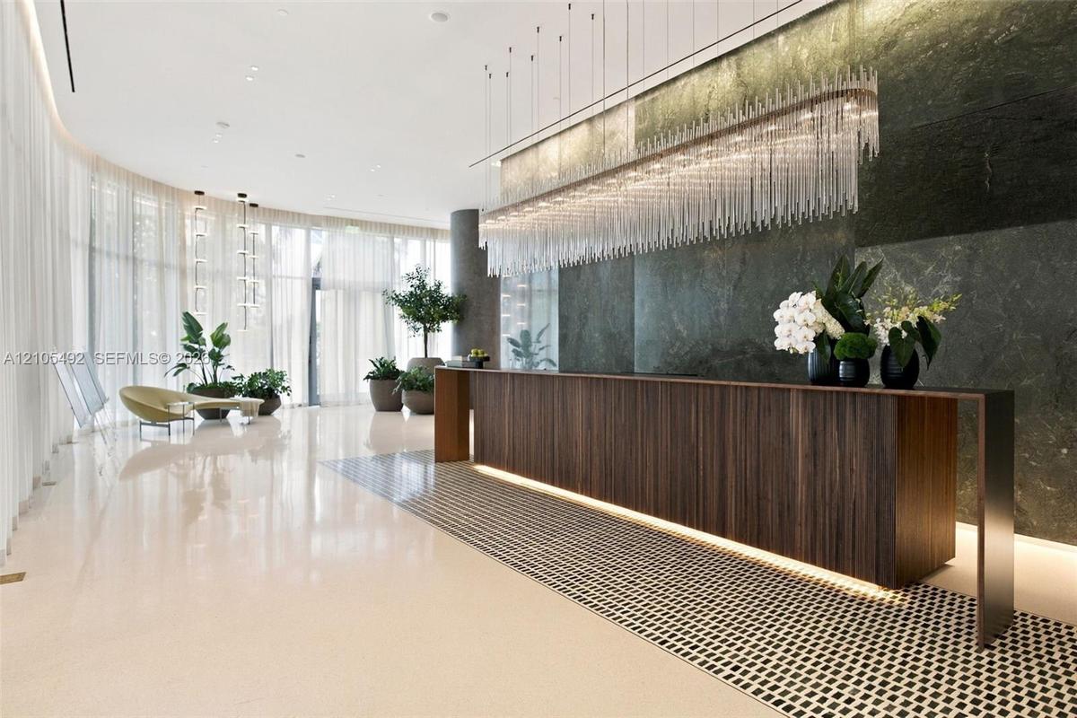 Floor-to-ceiling curved windows, polished light-toned stone flooring, dark wood-finish reception desk, large-scale stone wall cladding, and linear cry