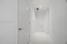 Interior corridor featuring smooth white walls, large-format tile flooring, recessed ceiling lighting, and solid-core doors with brushed-metal lever h