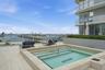 Elevated terrace featuring a tiled in-ground spa, large-format porcelain tile flooring, glass panel railing, and integrated privacy hedging