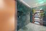 Floor-to-ceiling dark green stone wall tiling, integrated wood-finish shelving unit, oversized frosted glass door with metal pull handle, and stone ti