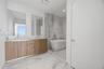 Double vanity featuring wood-finish cabinetry, solid-surface countertops, dual rectangular undermount sinks, and a glass-enclosed wet room with a free