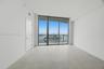 Floor-to-ceiling glass wall, large format tile flooring, and metal-framed balcony access with water and city skyline surroundings