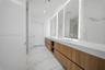Dual-sink floating vanity with wood-finish cabinetry, solid surface countertop, large-format tile wall surrounds, and integrated LED vanity mirrors