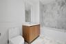 Bathroom featuring a wood-finish vanity with a white countertop, rectangular wall mirror, full-height stone-patterned tile shower surround, and white 