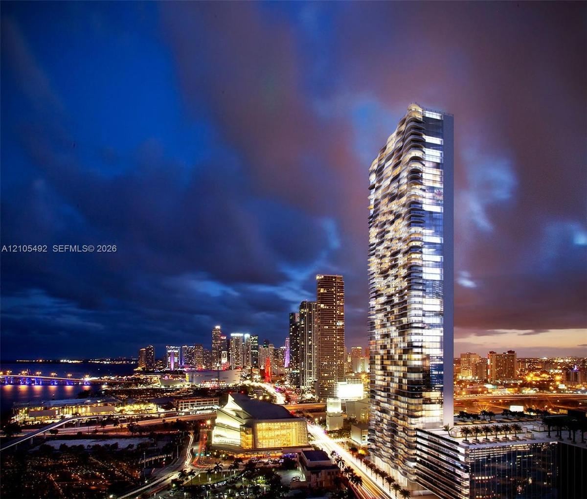 High-rise residential tower featuring a glass facade, recessed balconies, a tiered podium structure, and an illuminated exterior design