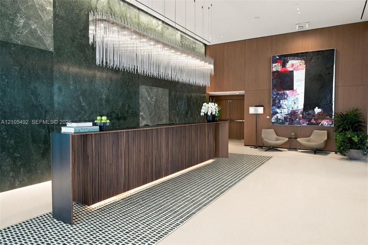 Grand lobby entrance featuring a polished stone feature wall, floor-to-ceiling wood-paneling, a custom wood-finish reception desk, and a linear tiered