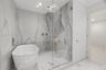 Freestanding soaking tub, frameless glass-enclosed shower, ceiling-mounted rainfall showerhead, and floor-to-ceiling stone-finish tile surround
