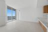 Floor-to-ceiling windows, light-tone tile flooring, stone-finish countertops, wood-finish cabinetry, and attached balcony