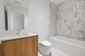 Bathroom featuring a wood-finish vanity with a rectangular sink, stone-surface countertop, floor-to-ceiling tile surround, and a deep soaking tub