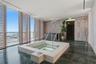 Sunken jetted tub with integrated handrails, floor-to-ceiling glass paneling, wood-slat privacy screening, polished stone flooring, and wall-mounted s
