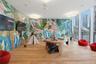 Expansive room featuring floor-to-ceiling windows, wood-finish flooring, vibrant jungle-themed wall murals, and geometric recessed ceiling lighting