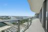 Curved private balcony featuring oversized porcelain tile flooring, glass panel railings, and expansive water and urban scenery