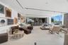 Open-concept living area featuring light-toned tile flooring, floor-to-ceiling windows, modern track lighting, and a built-in bar with stone-finish su