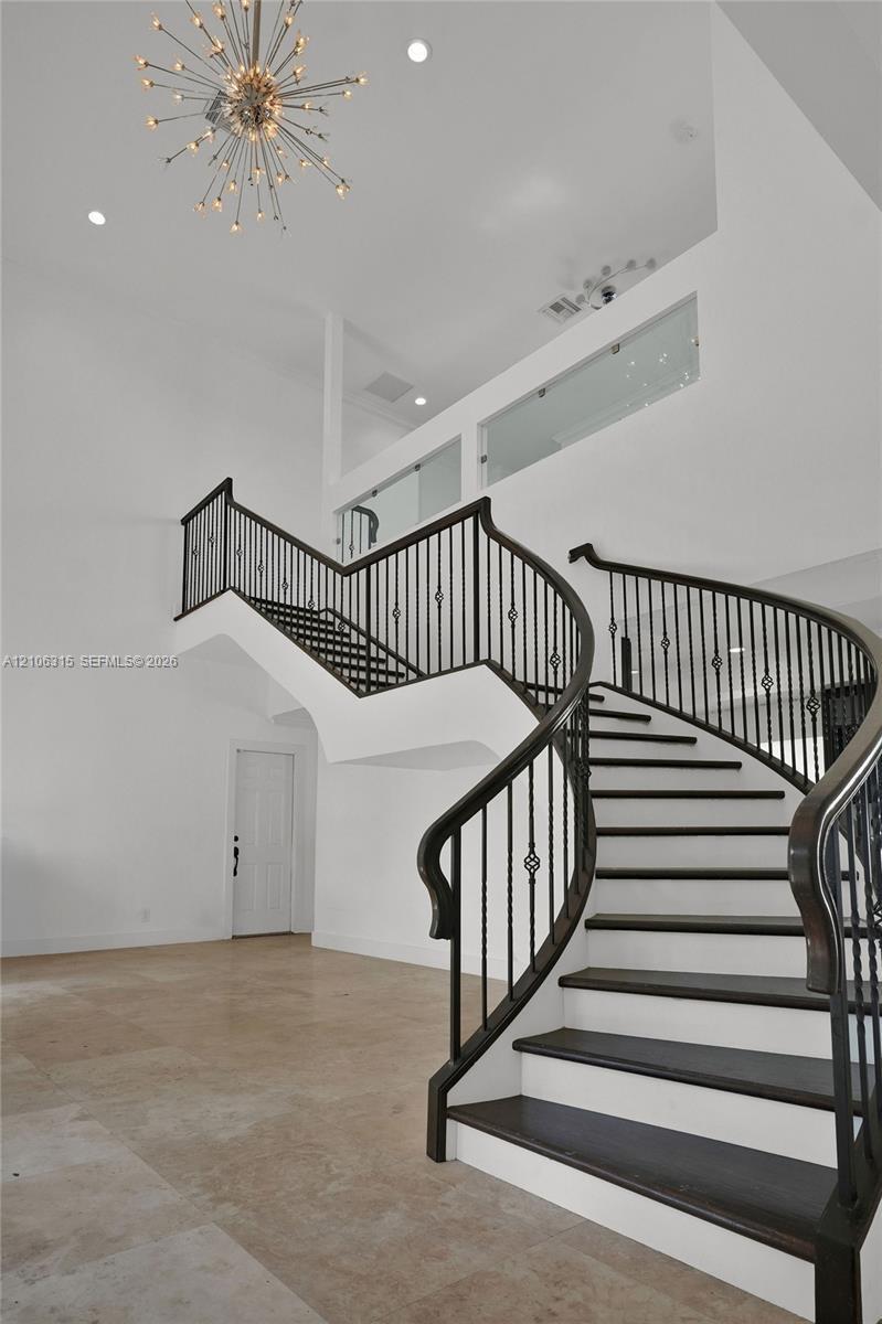 Curved staircase featuring dark-finished treads, white risers, and decorative metal balusters, complemented by high ceilings, a starburst chandelier, 