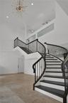 Curved staircase featuring dark-finished treads, white risers, and decorative metal balusters, complemented by high ceilings, a starburst chandelier, 