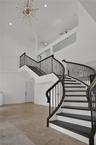 Curved staircase with dark-finished wood treads and metal balusters, polished tile flooring, double-height ceiling, glass-panel balcony railing, and s