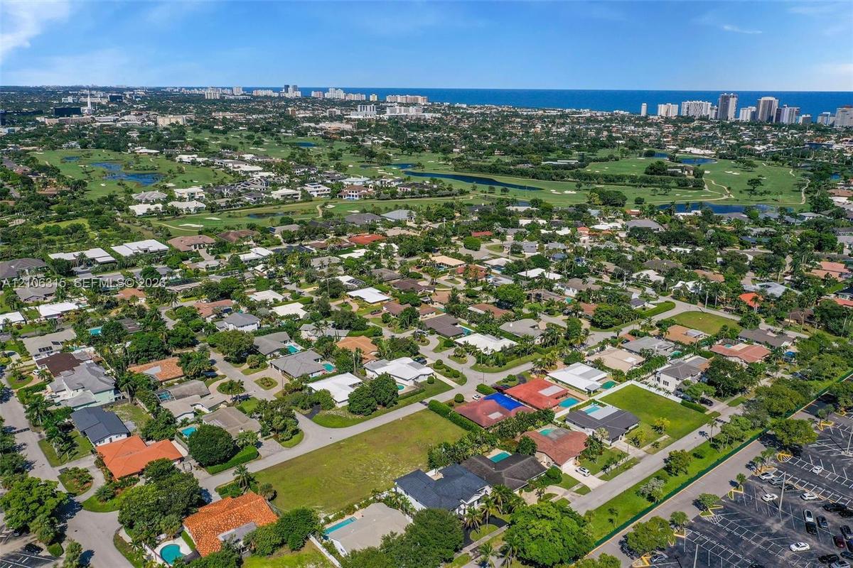 Aerial perspective of a residential neighborhood featuring expansive green space, mature landscaping, and proximity to the coastline