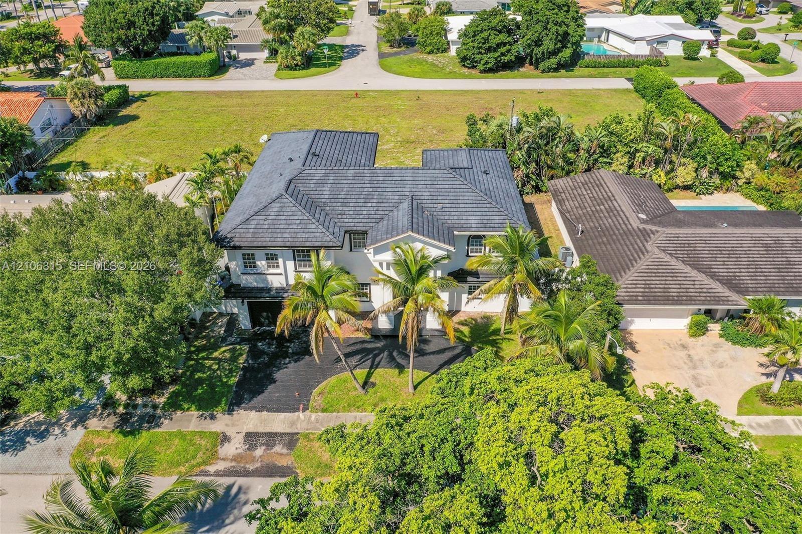 Two-story residence featuring a dark-toned tile roof, exterior white cladding, multiple mature palm trees, and a paved driveway