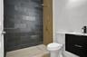 Walk-in shower featuring dark stone-style tile, gold-finish hardware, and a wood-finish panel accent, paired with a black floating vanity and integrat