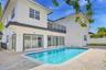 Two-story exterior featuring white stucco finish, second-level balcony with metal railing, multiple sliding glass doors, and a rectangular swimming po