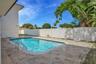 In-ground swimming pool with metal ladder, surrounded by stone paver patio and enclosed by a solid vinyl privacy fence