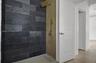 Walk-in shower featuring charcoal-toned stone tile, vertical wood-finish paneling, brushed metallic rainfall shower head with handheld sprayer, and a 