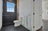 Walk-in shower enclosure with large-format dark tile, wall-mounted rain shower head, dual-pane grid window, and wood-finish flooring