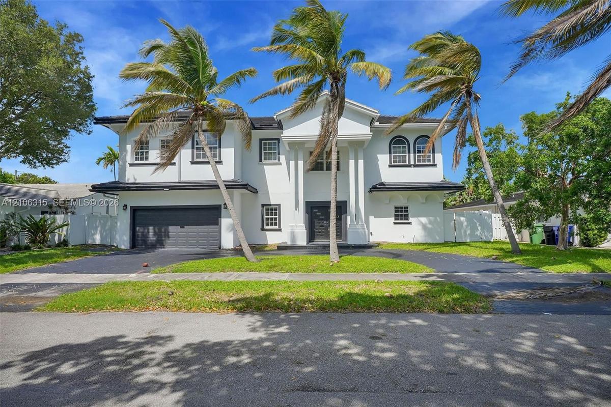 Two-story residence featuring a central portico with classical columns, stucco exterior, arched upper windows, and a paved driveway leading to an atta