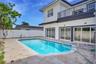 Exterior featuring a white stucco facade, private swimming pool, stone paver decking, white vinyl perimeter fencing, and an upper-level balcony with m