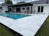 Outdoor swimming pool with a black-framed pergola, white tiled pool deck, and white exterior stucco finish