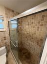 Enclosed shower with tiled walls and floor, featuring a glass sliding door and a shower head with an attached sprayer