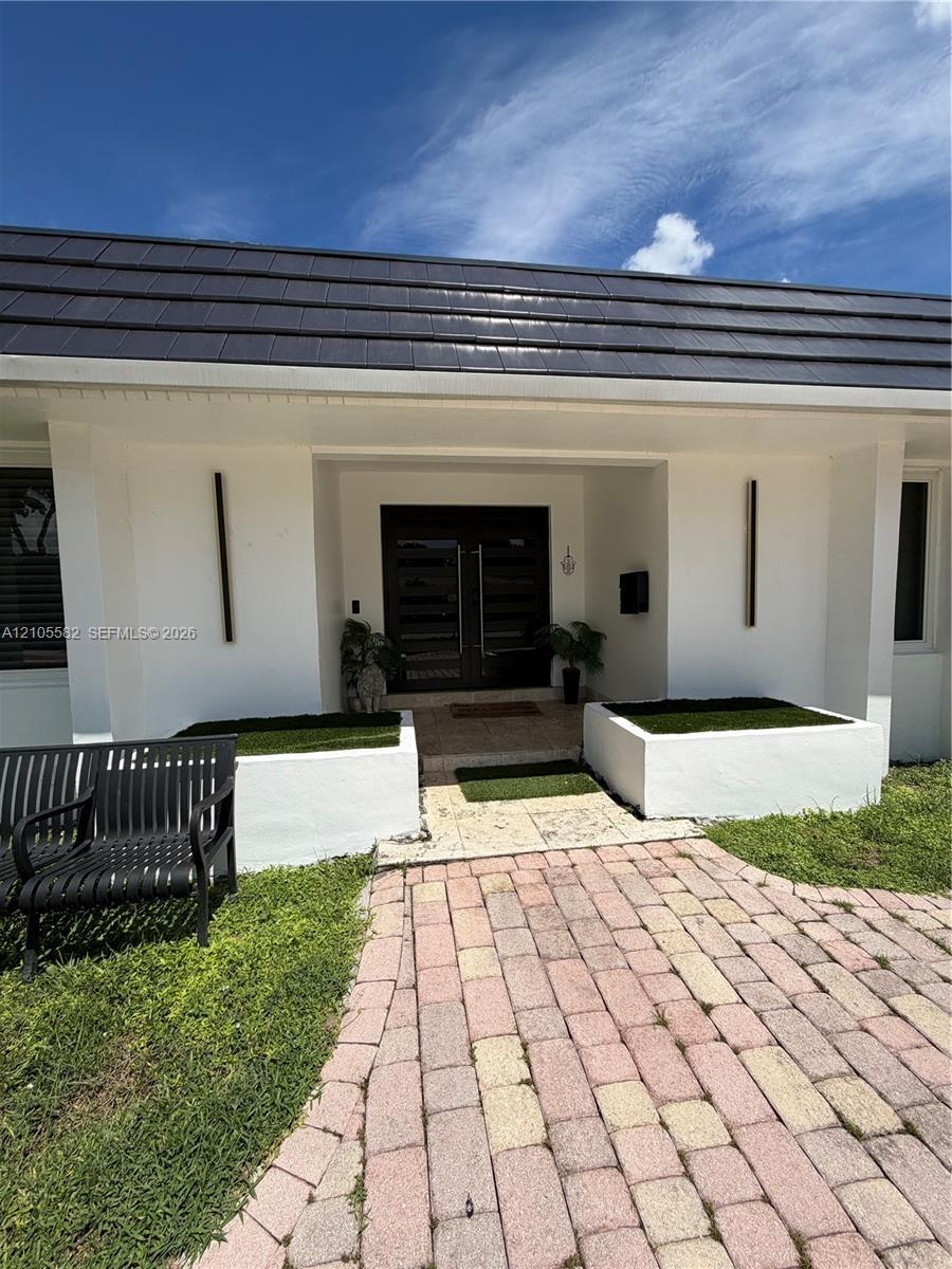 White exterior with a dark tile roof, paved brick walkway, and built-in planters
