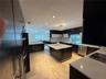 Gourmet kitchen featuring a large central island, light-toned stone tile flooring, sleek dark cabinetry, and white countertops