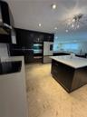 Contemporary kitchen featuring sleek dark cabinetry, integrated stainless steel appliances, a central island with a white countertop, and recessed lig