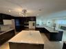 Spacious kitchen featuring dark cabinetry, expansive light-toned countertops, a multi-tiered island, and recessed lighting
